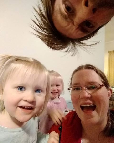 Mother and young daughters smile at camera with father looking into frame from above