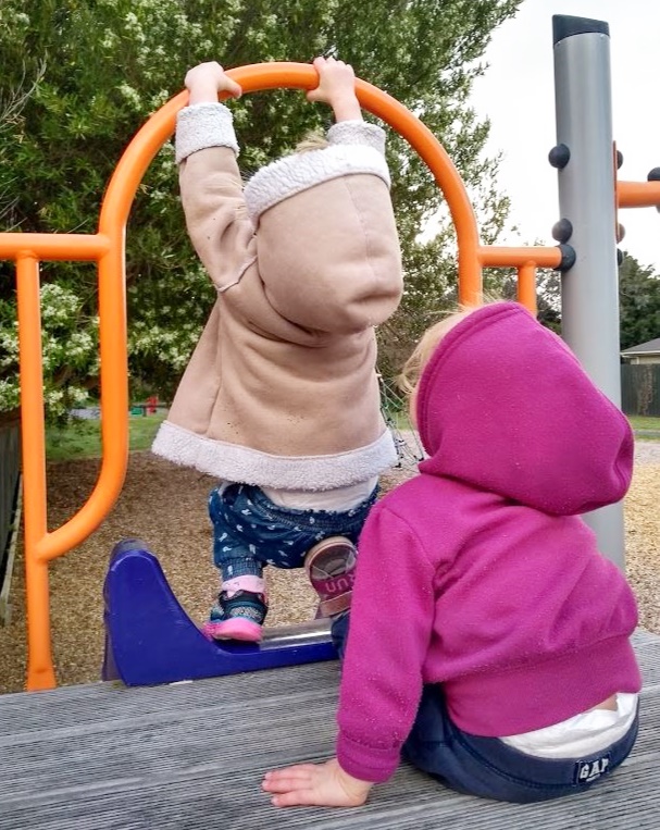 Children in hoodies playing on playground platform above slide