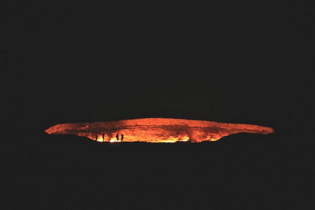 door to hell burning cave with people standing on edge at night